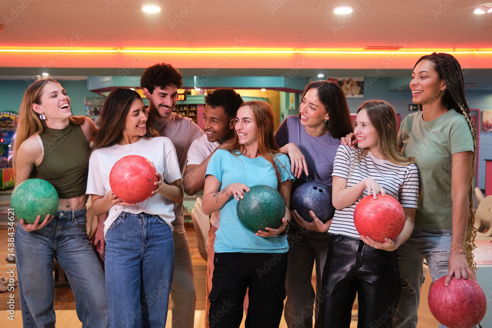 Group of young adults having fun bowling together, holding colorful bowling balls and smiling