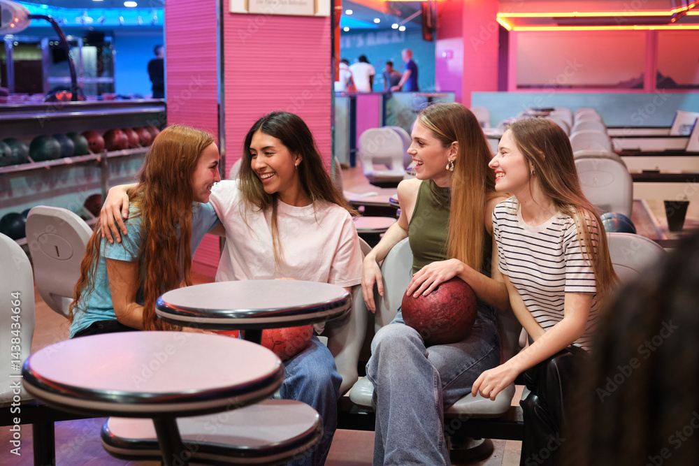 Four cheerful female friends enjoying their time together, chatting and laughing while sitting in a bowling alley