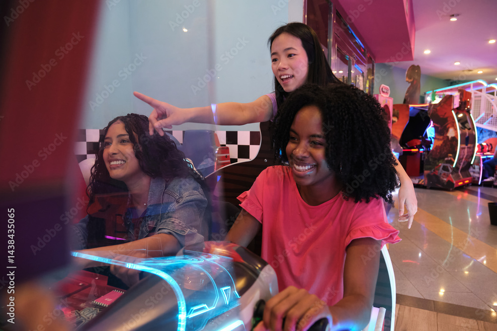 Three young women having fun playing a car racing arcade game in an amusement park
