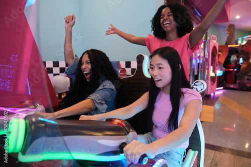Obraz na płótnie Group of diverse young women having fun while playing arcade racing game in entertainment center w salonie