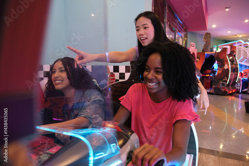 Three young women having fun playing a car racing arcade game in an amusement park