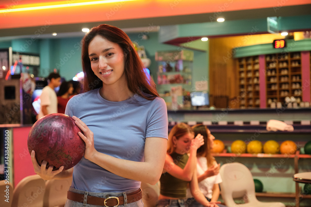 Young woman holding a bowling ball, smiling in a bowling alley, ready to play