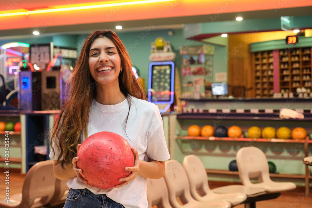 Happy young woman holding a bowling ball and smiling in a bowling alley