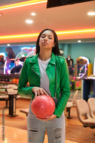 Obraz na płótnie Stylish young bowler holding a red bowling ball in a bowling alley, ready for a game w salonie