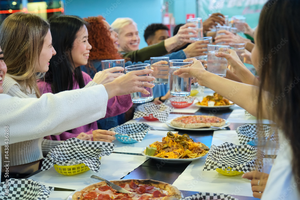 Group of young cheerful people enjoying a meal together, toasting with water and celebrating friendship in a pizzeria