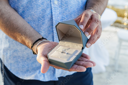 Elegant engagement ring in a modern geometric black box placed on the sand. Romantic beach setting at sunset, symbolizing a marriage proposal, love, and commitment. Perfect for themes of luxury, roman