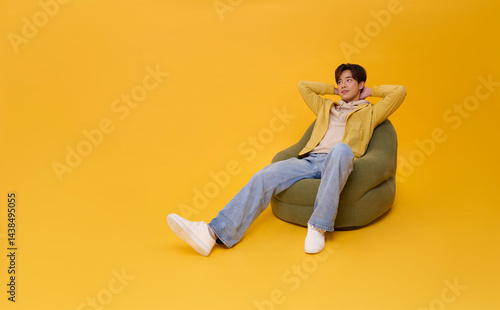 Full body Happy smiling young asian handsome man relaxing sitting on sofa isolated on yellow background. Lifestyle concept