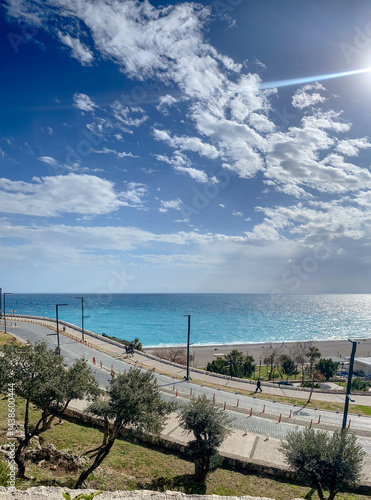 Obraz na plátně Seaside promenade with turquoise sea, coastal road and dramatic blue sky on a su