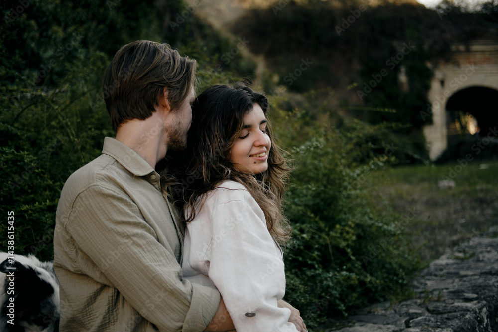 Naklejka premium Close-up portrait of a young smiling couple embracing outdoors, surrounded by lush greenery. Natural and authentic love story moment. Woman and man in love on date in park.