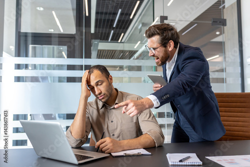Obraz na płótnie A frustrated manager confronts a stressed employee in an office setting, pointing at a laptop. The scene depicts a work-related conflict between colleagues. w salonie