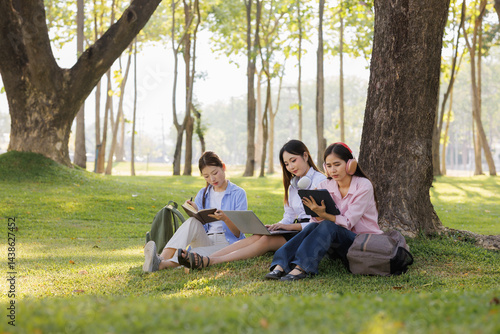 A group of female students sits under a tree in the park, laughing and chatting joyfully together.