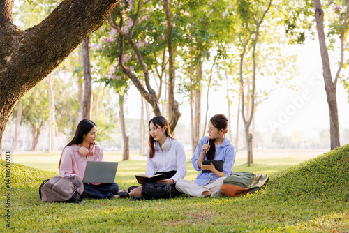 A group of female students sits under a tree in the park, laughing and chatting joyfully together.