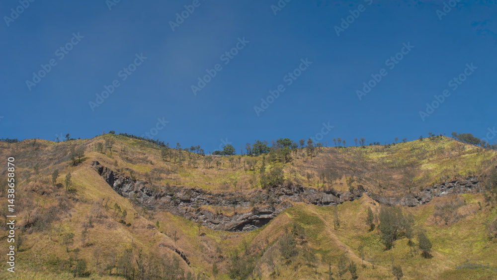 Cliff landscape at Mount Bromo highlands, East Java, Indonesia. Rocky slope with dry grass and trees under clear blue sky. Popular nature destination for traveling and outdoor adventure.
Cliff landscape at Mount Bromo highlands, East Java, Indonesia. Rocky slope with dry grass and trees under clear blue sky. Popular nature destination for traveling and outdoor adventure.