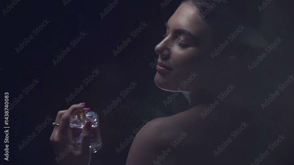 Perfume. Beauty glamour fashion woman applying Perfume. Beautiful model girl holding bottle of perfume on dark background, enjoying aromatic, scented water. Perfumery concept. Spray. Slow motion.