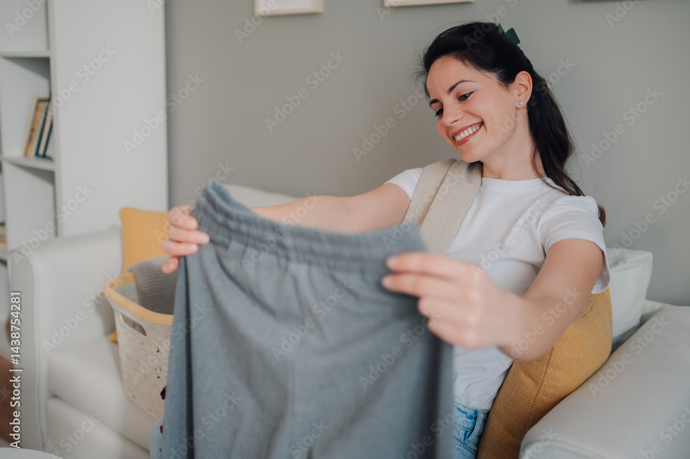 Obraz premium Woman folding laundry smiling and sitting on sofa at home