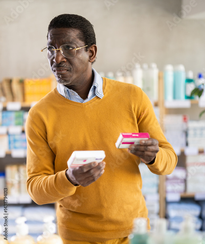 Obraz na płótnie African man choose buy painkiller paracetamol tablet at pharmacy, compare with other good. Client check for absence of harmful substances, view product in details. w salonie
