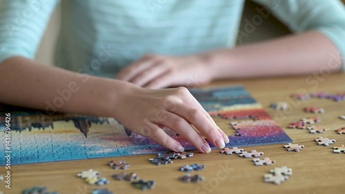 Close-up view of young woman hands assembling puzzles at home. Connecting jigsaw puzzle pieces, assembling a jigsaw puzzle. Fun family leisure. Table games, home relaxation. Slow motion footage.