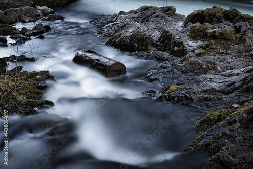 Long exposure of a tranquil mountain stream flowing over dark mossy rocks with a driftwood log
