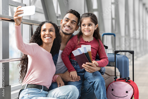 Airport Selfie. Happy Middle Eastern Family Of Three Taking Photo With Smartphone While Waiting For Flight At Terminal, Cheerful Arabic Parents And Daughter Smiling And Posing At Camera, Free Space