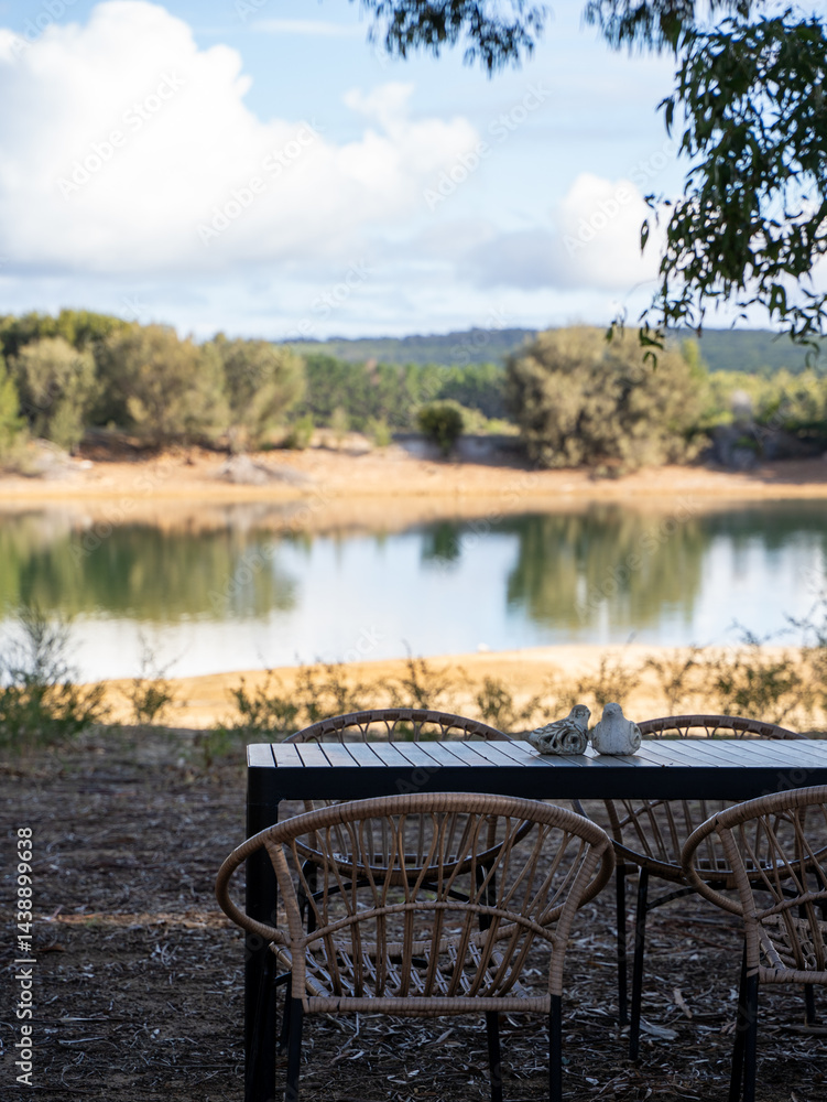 Fototapeta premium Outdoor dining setup by a calm lake with distant trees and clouds