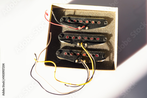 Obraz na płótnie Three black single-coil guitar pickups with red pole pieces sit in a foam-lined box, casting shadows on surface. Wires extend from each pickup, ready for wiring into an electric guitar w salonie