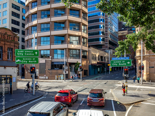 Photography Elevated view in Sydney, Australia downtown intersection featuring modern office buildings, directional signs, vehicles, and pedestrians waiting at a traffic light in an urban business district