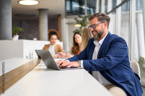 Focused male lawyer working on laptop in boardroom while female colleagues collaborate in the background