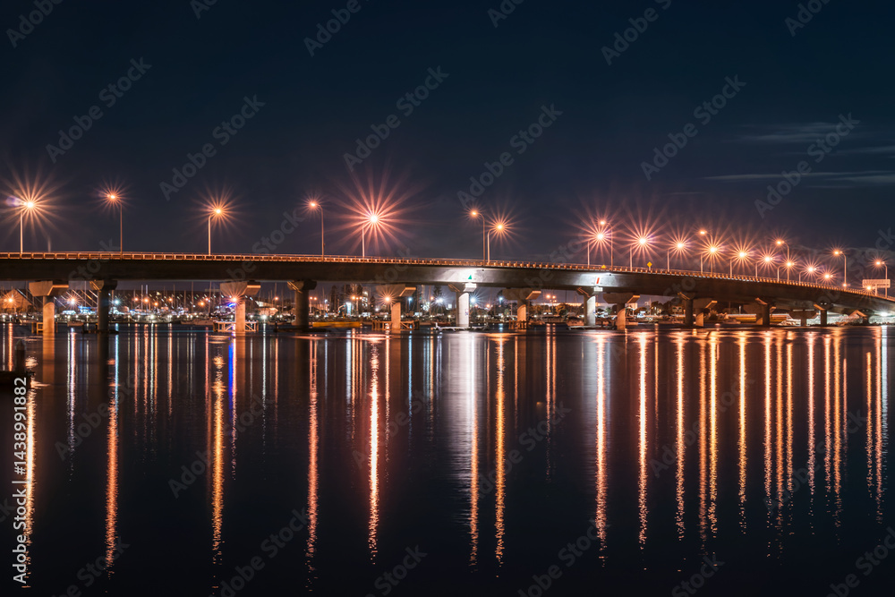 Tauranga harbour bridge curves across bay illuminated at night worth star-bursts from street lights.