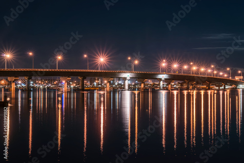 Obraz na płótnie Tauranga harbour bridge curves across bay illuminated at night worth star-bursts from street lights. w salonie