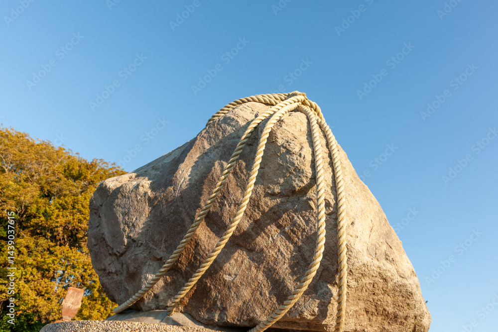 Large rock with ropes tied around against blue sky