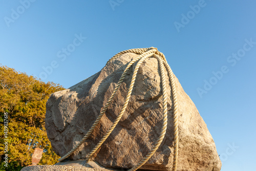 Large rock with ropes tied around against blue sky