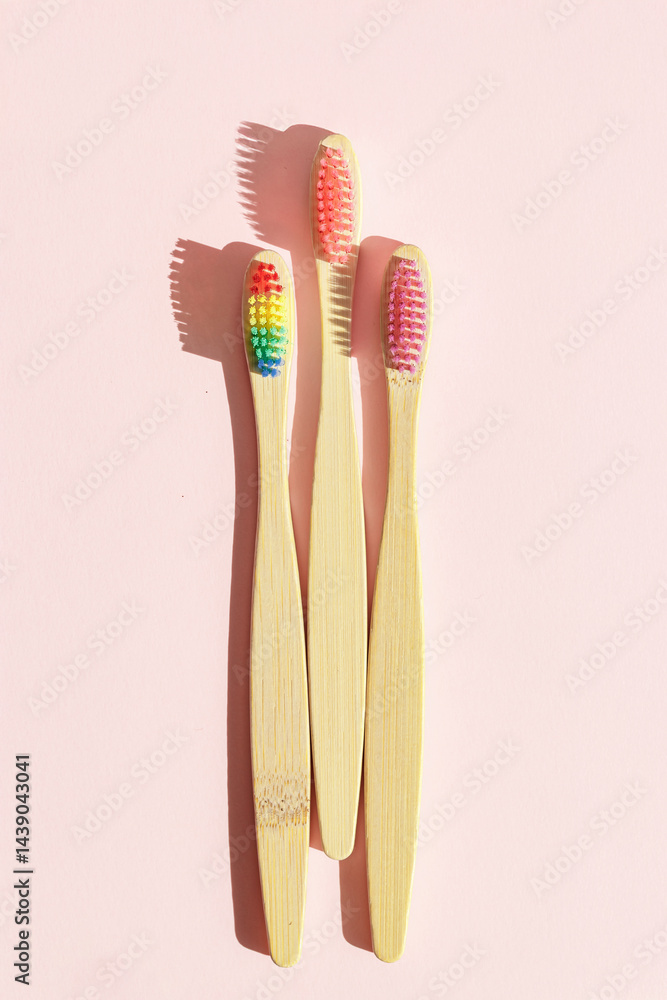 Closeup Aesthetic Beige bamboo toothbrushes with colors bristles at sunlight on pink pastel background. Simplicity, hygiene, and environmentally friendly alternatives, top view photo, minimal flatly