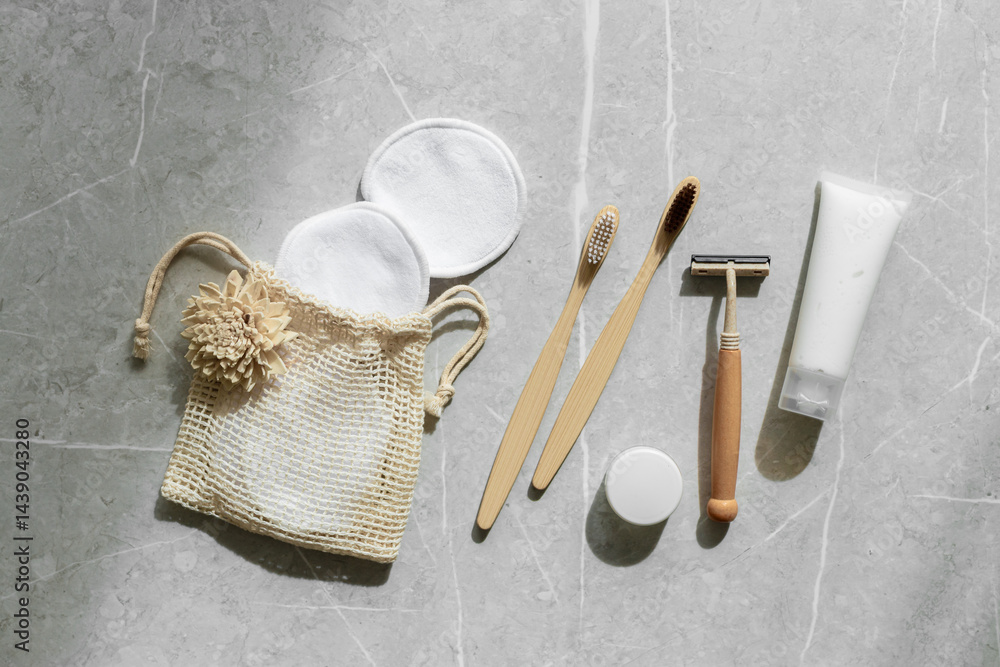 Hygiene products as bamboo toothbrushes, toothpaste, reusable pads, safety razor on grey marble background with natural light, eco-friendly items for self care, zero waste concept. Minimal top view