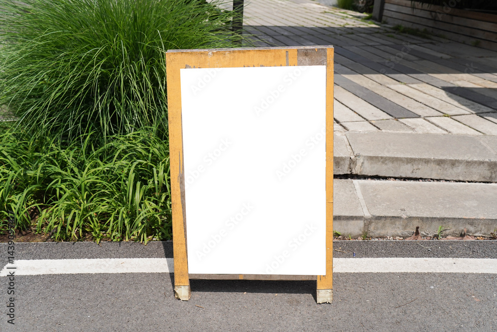 Blank white outdoor advertising stand sandwich board mock up template. Clear street signage board placed by an outdoor dinning area of a restaurant.