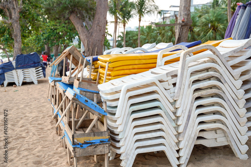 Obraz na płótnie Stacked white and yellow plastic beach chairs on sandy ground with wooden tables, tropical trees and relaxed atmosphere w salonie