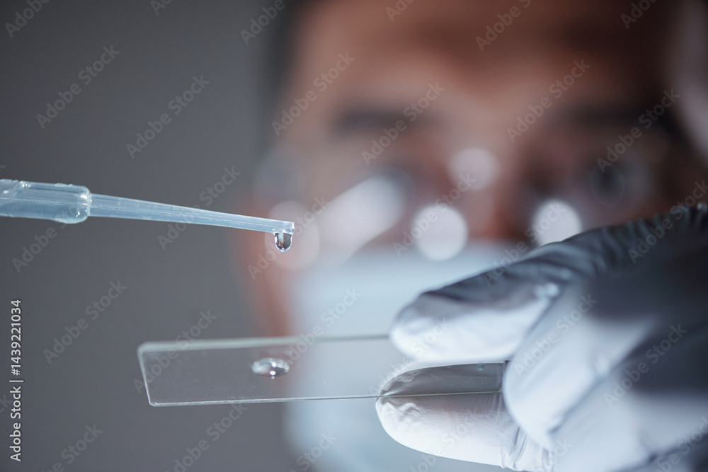 Focused scientist examining a glass slide with a pipette. Detailed scientific procedure being carried out with precision and attention in modern laboratory environment