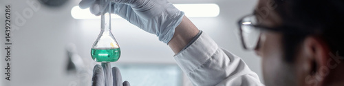 Technician wearing gloves is holding a beaker with green liquid in modern laboratory environment, focusing on conducting precise scientific experiment