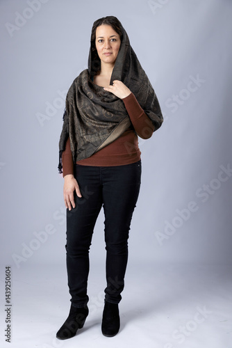 A  dark-haired woman wearing black pants, a brown top and a woven paisley shawl draped over her shoulder and head