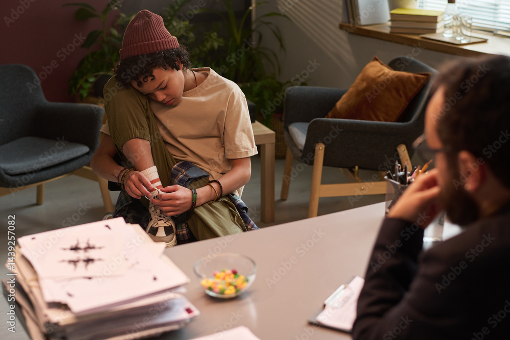 Problem schoolchild sitting in front of psychologist and tying shoelaces on his sneakers while counselor looking at him
