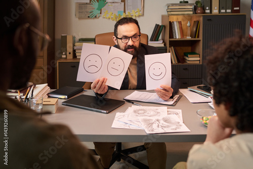 Obraz na płótnie Confident psychologist talking to schoolchild and asking him choose one of three different emotions illustrated on papers w salonie
