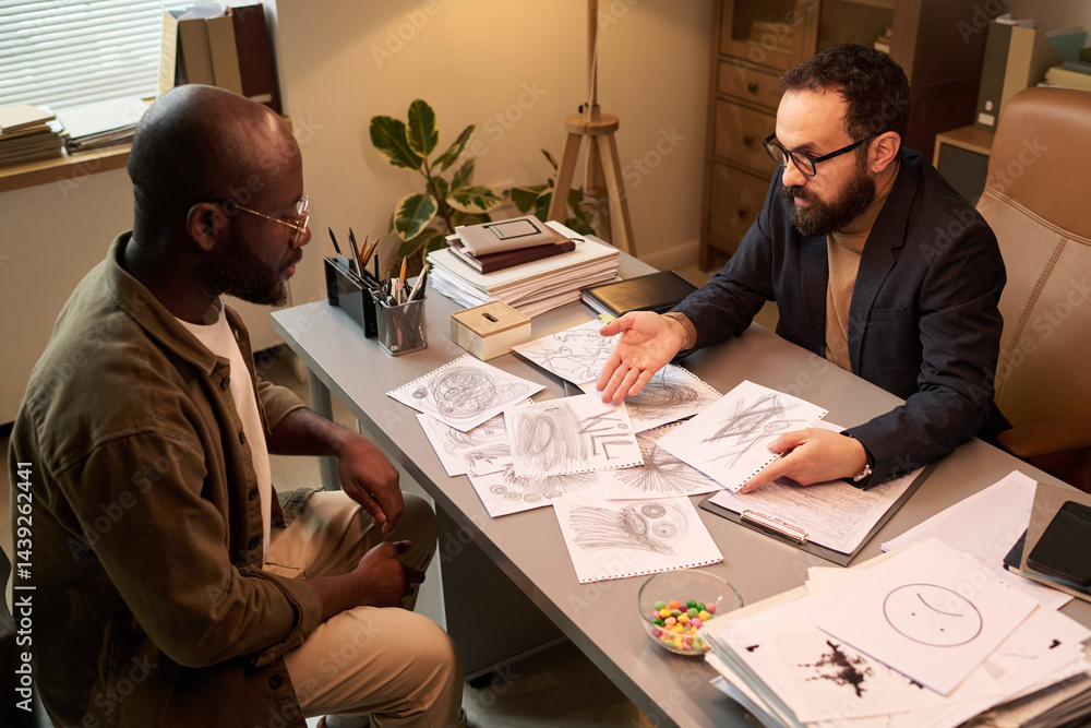 Psychologist showing drawings of schoolchild to his father while analyzing symbols illustrated by troublemaking kid
