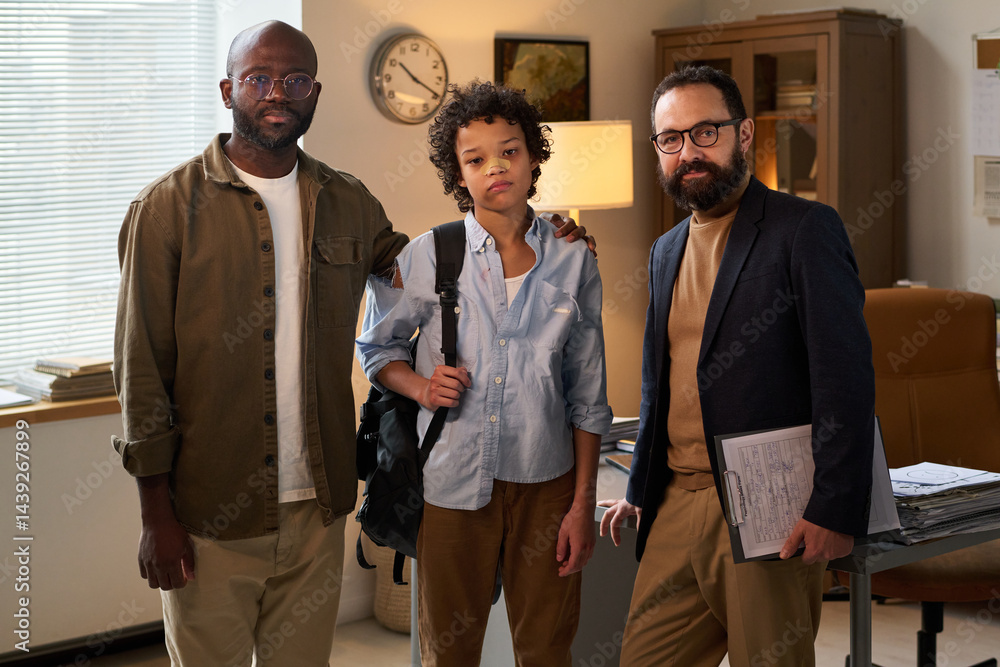 Psychologist with document standing next to schoolboy with broken nose and his father while everyone looking at camera