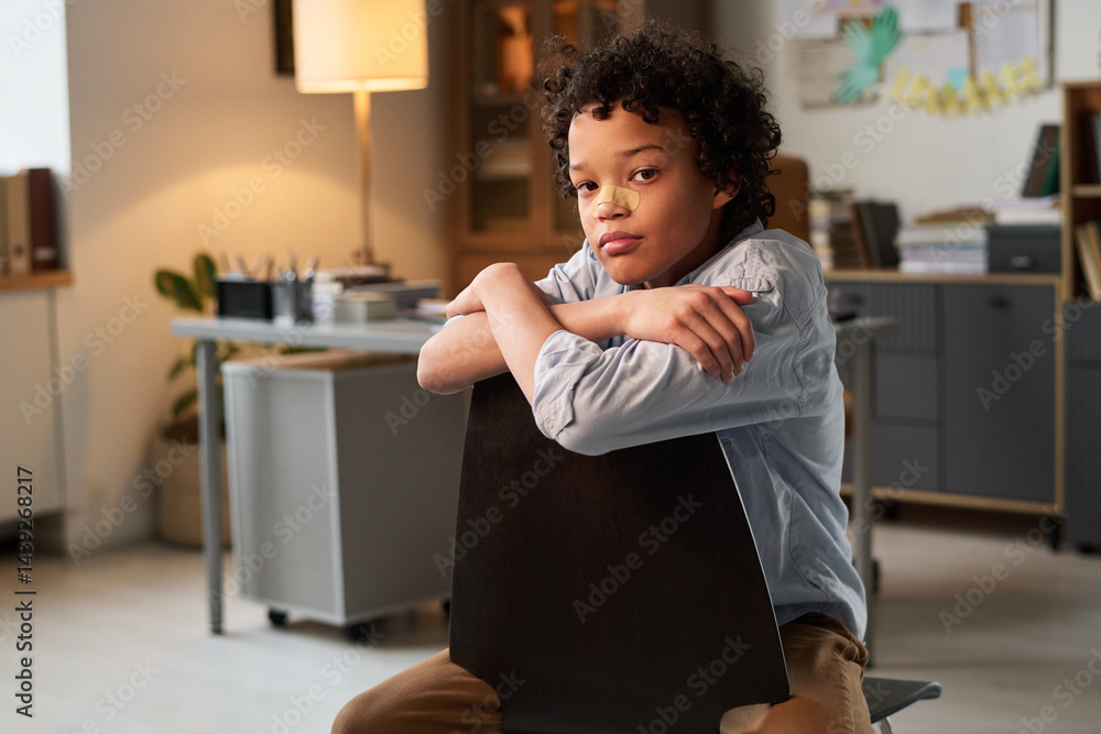 African American schoolboy looking at camera after fighting with classmates while sitting in office of school psychologist