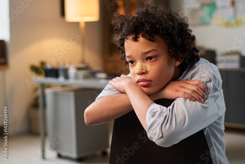 Obraz na płótnie Sulky African American boy with bandage on nose sitting on chair in psychologist office and thinking of his behavior w salonie