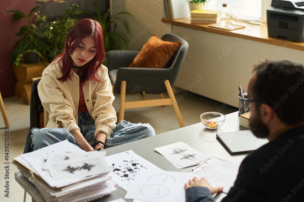Adolescent girl sitting in armchair in front of school psychologist during their conversation about patient problems in office