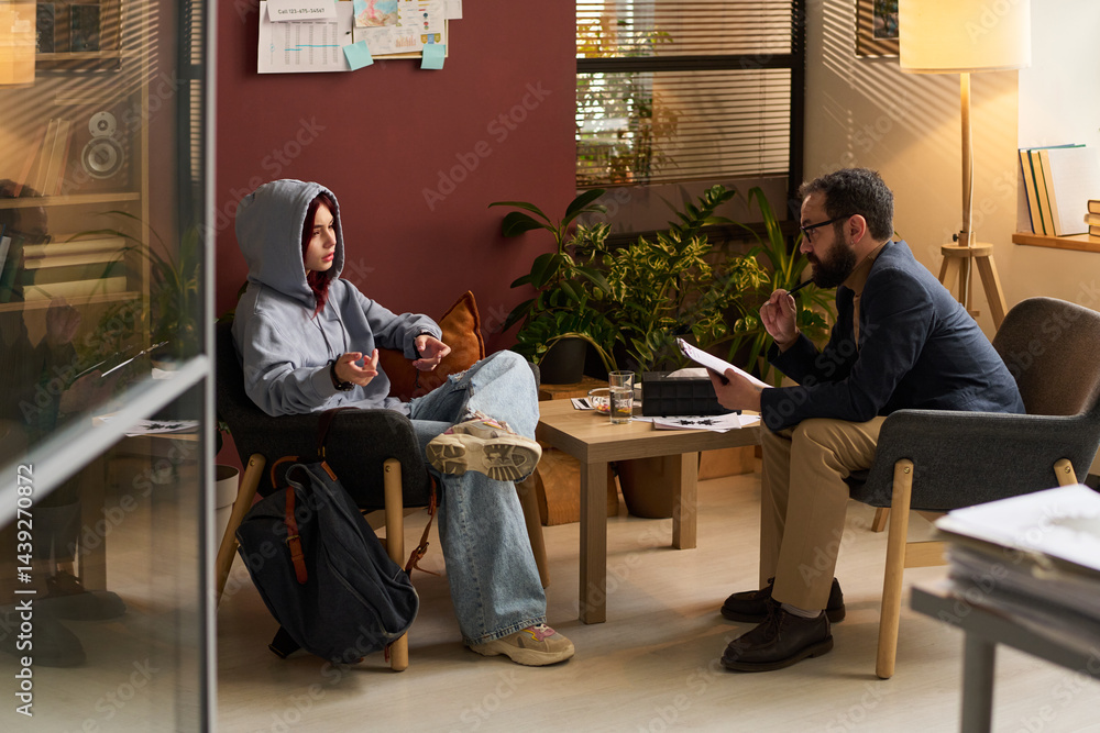 Confident school psychologist and teenage patient sitting in armchairs in front of one another during psychological session