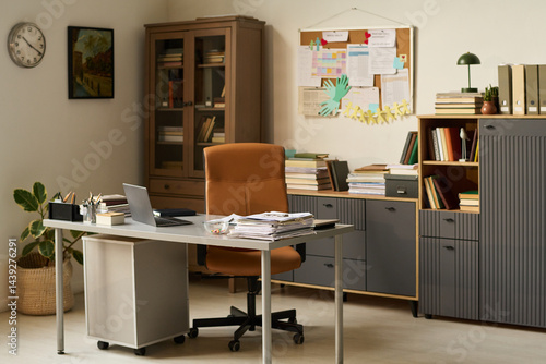 Workplace of modern school psychologist with armchair standing in front of desk with paper documents, laptop and other supplies