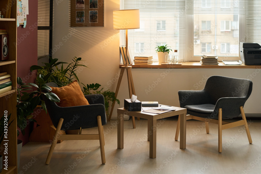 Small square table with box of tissues, paper documents and notepad of psychologist standing between two armchairs in office