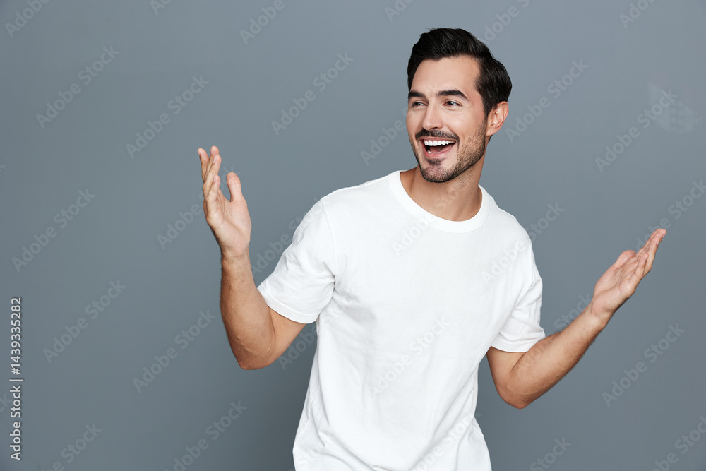 Smiling happy cheerful young man wearing a white t-shirt gestures with open hands, expressing joy and excitement against a grey background. Positive lifestyle concept. Smiling happy cheerful young man wearing a white t-shirt gestures with open hands, expressing joy and excitement against a grey background. Positive lifestyle concept.