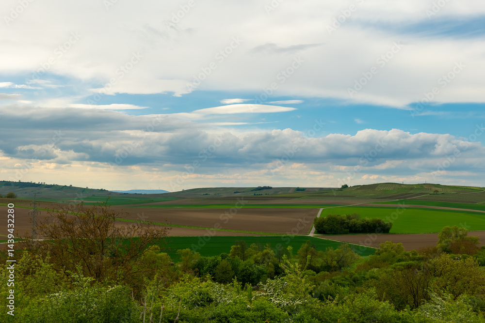 Obraz premium Expansive countryside landscape featuring rolling hills and vibrant green fields under a cloudy sky